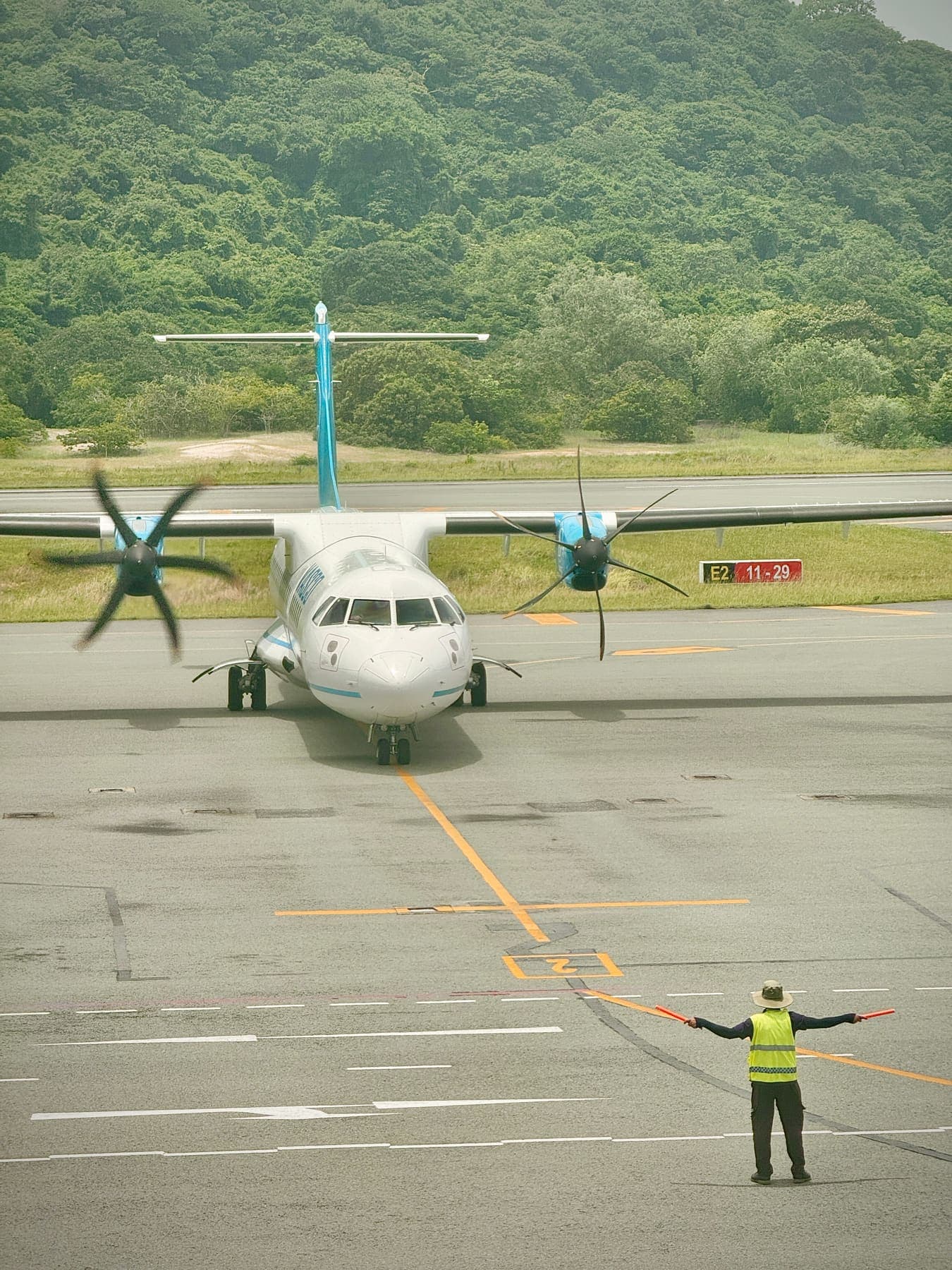 A ground marshal guiding a propeller plane on the island runway