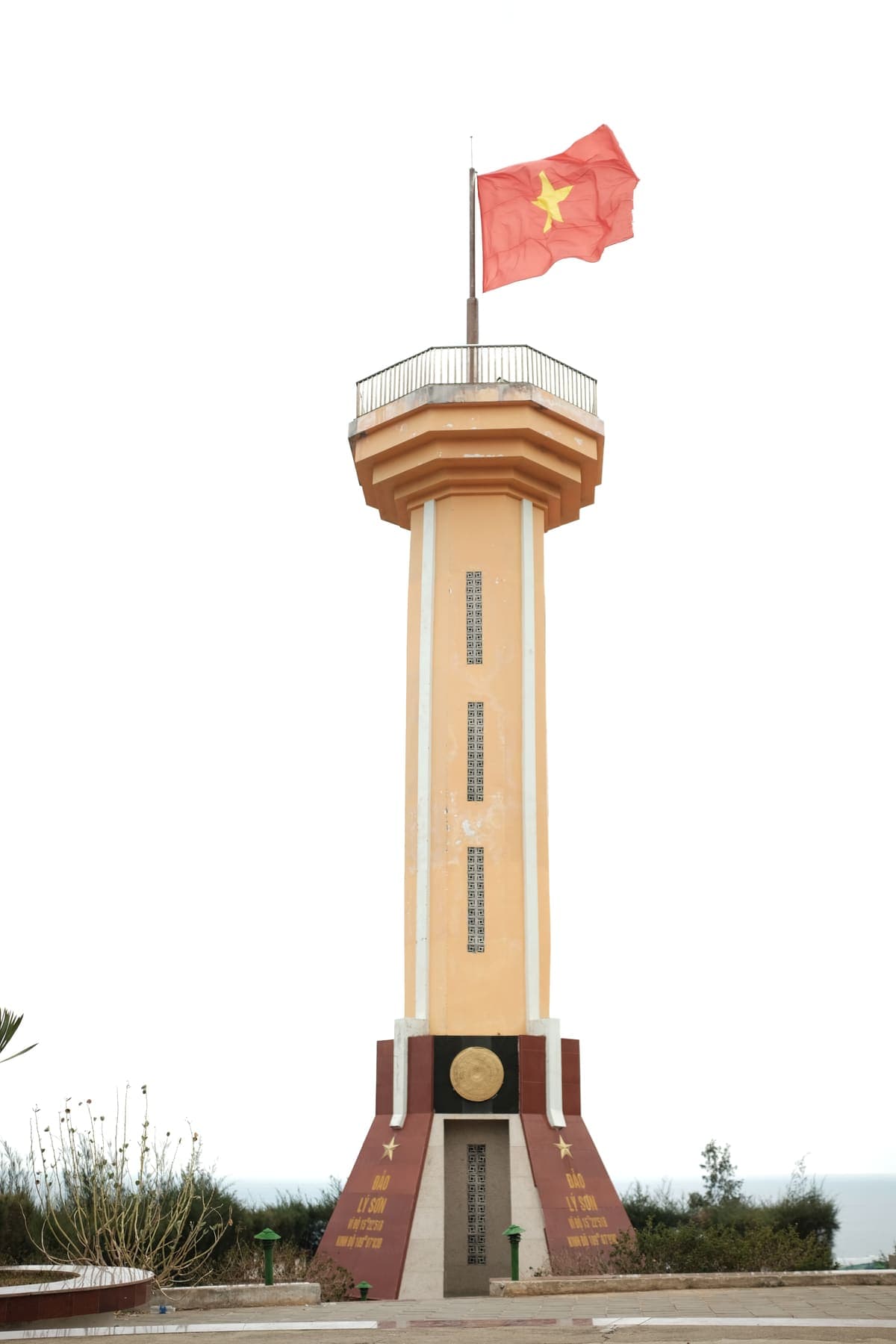 A tall flag tower with the Vietnamese flag against a white sky