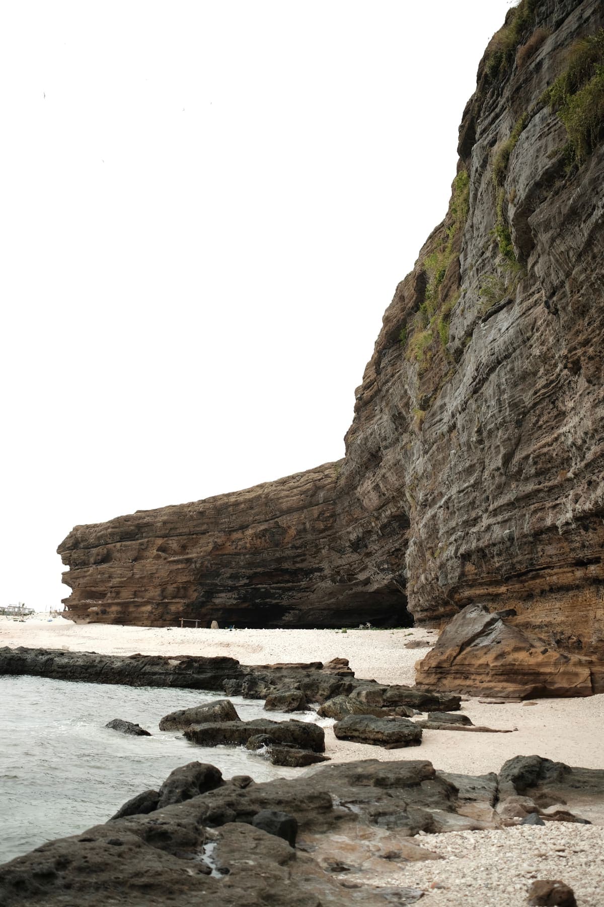 A rocky beach beneath a tall, layered sea cliff