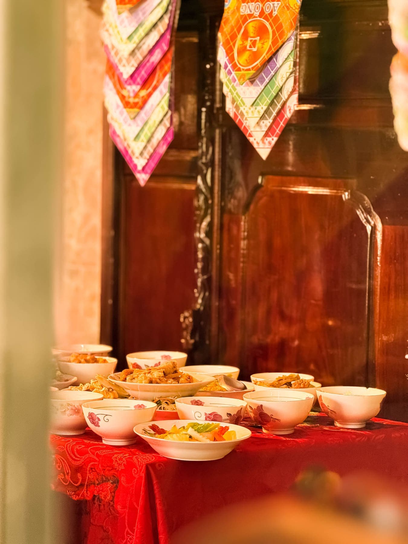 Bowls of food on a red cloth beneath hanging paper offerings