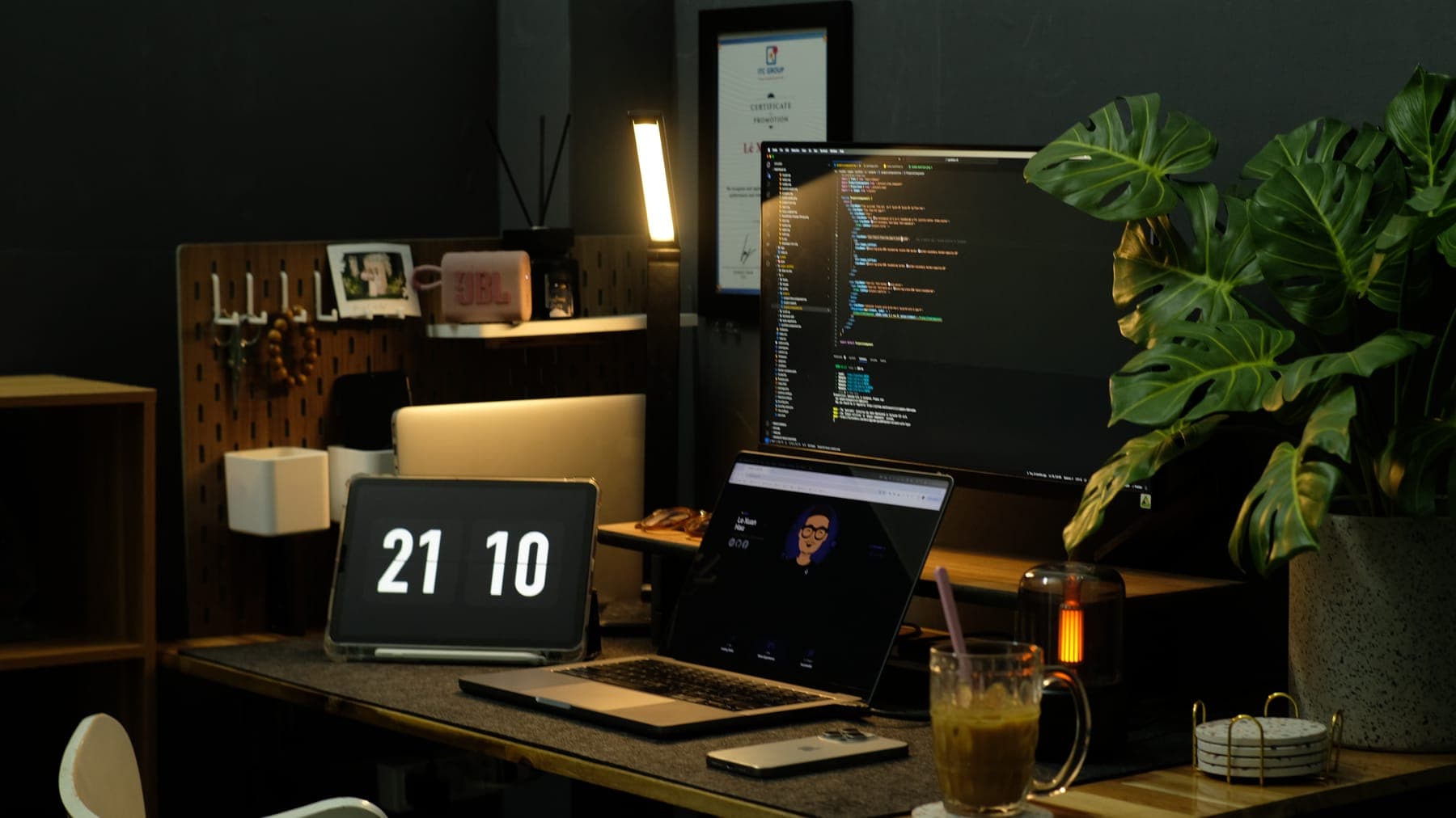 Code on the monitor above a laptop and a flip clock at 21:10